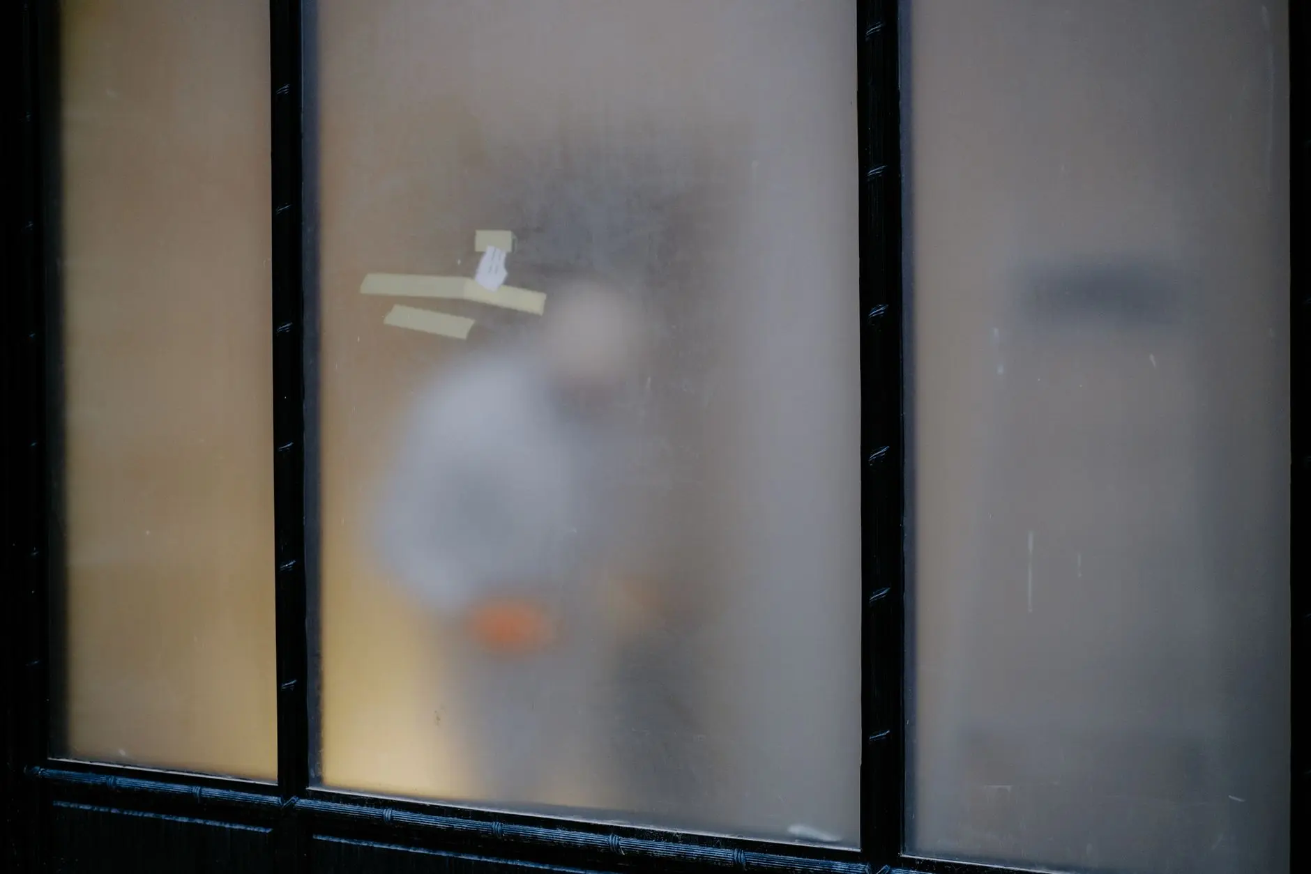 Blurry silhouette of a person seen through frosted glass with taped sections and black framing.