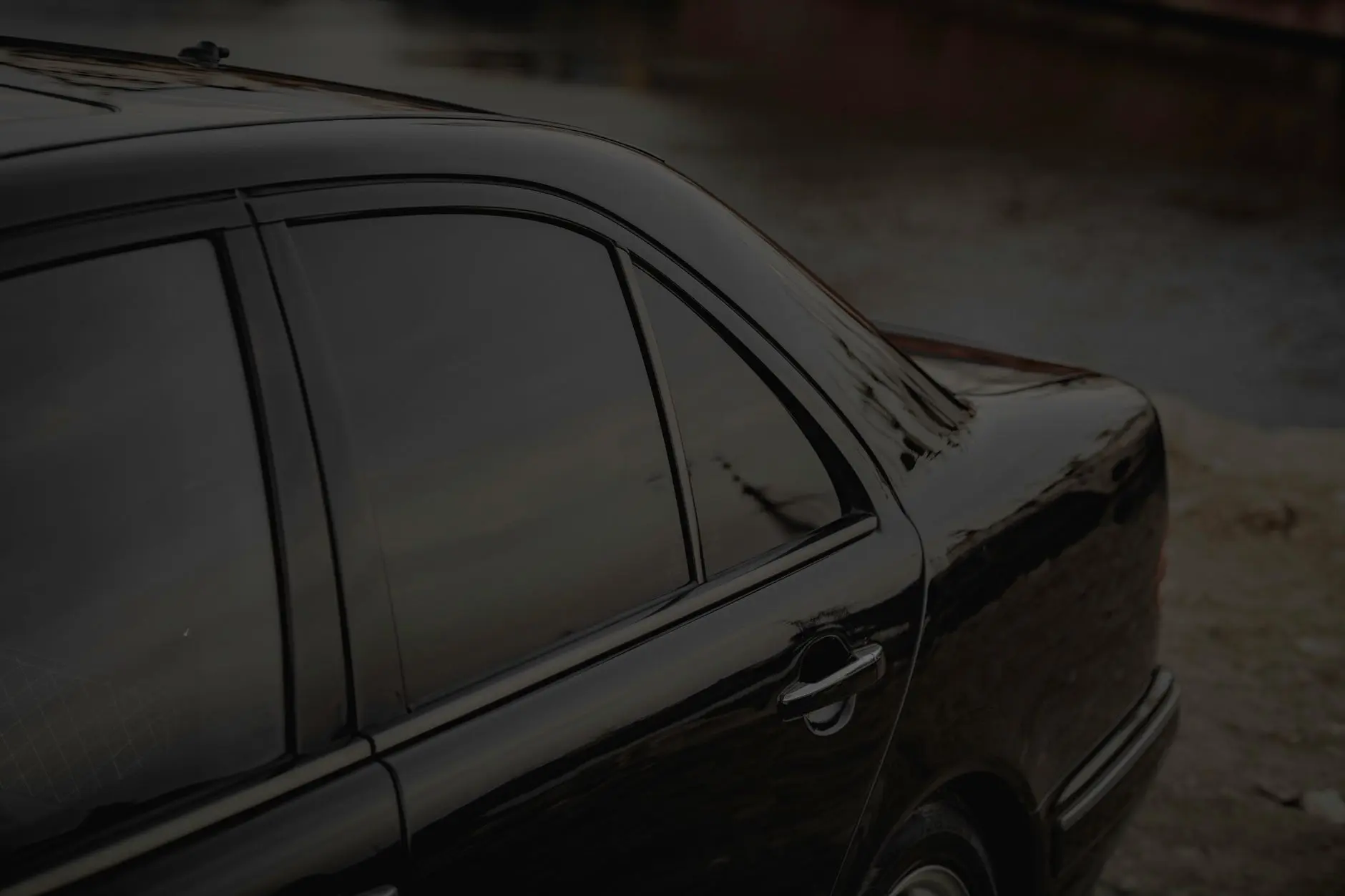 Close-up of a black car's side view with tinted windows by a calm riverbank.