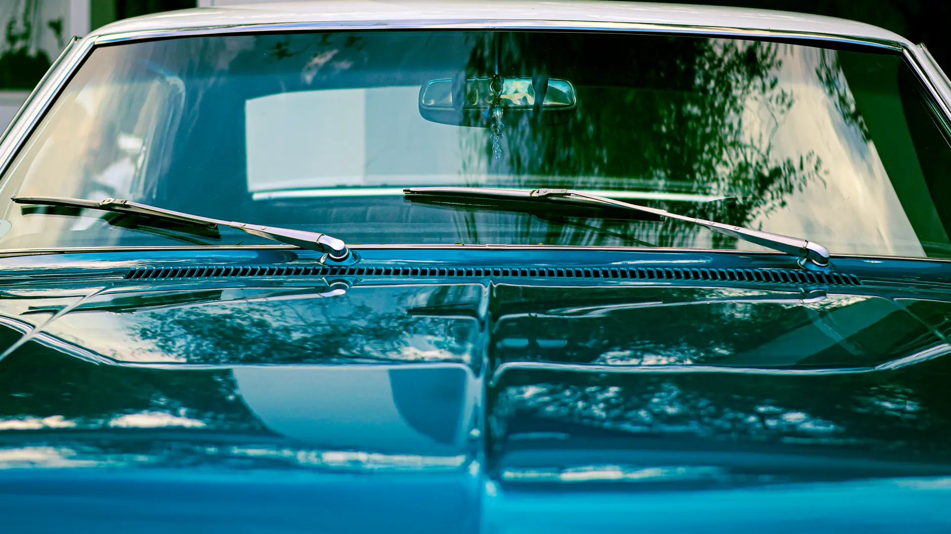 A close-up view of a classic blue vintage car windshield with reflections.