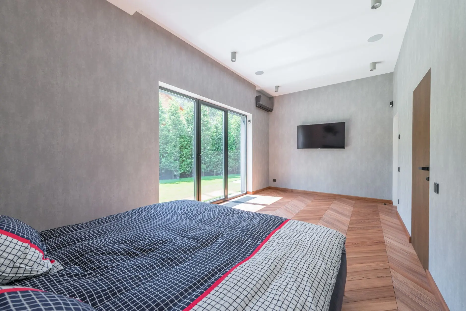 Bright and cozy minimalist bedroom with large sliding glass doors and wooden flooring.